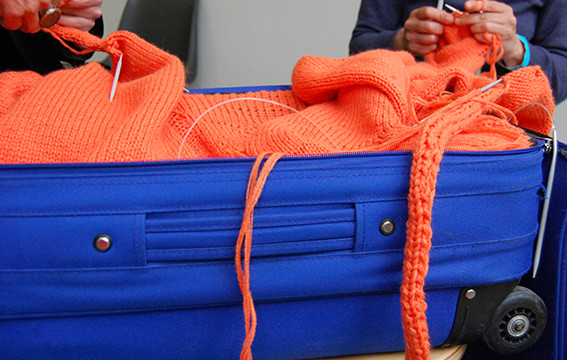 aus dem blauen Rollkoffer drängt eine orangefarbene Wollplastik in den Raum